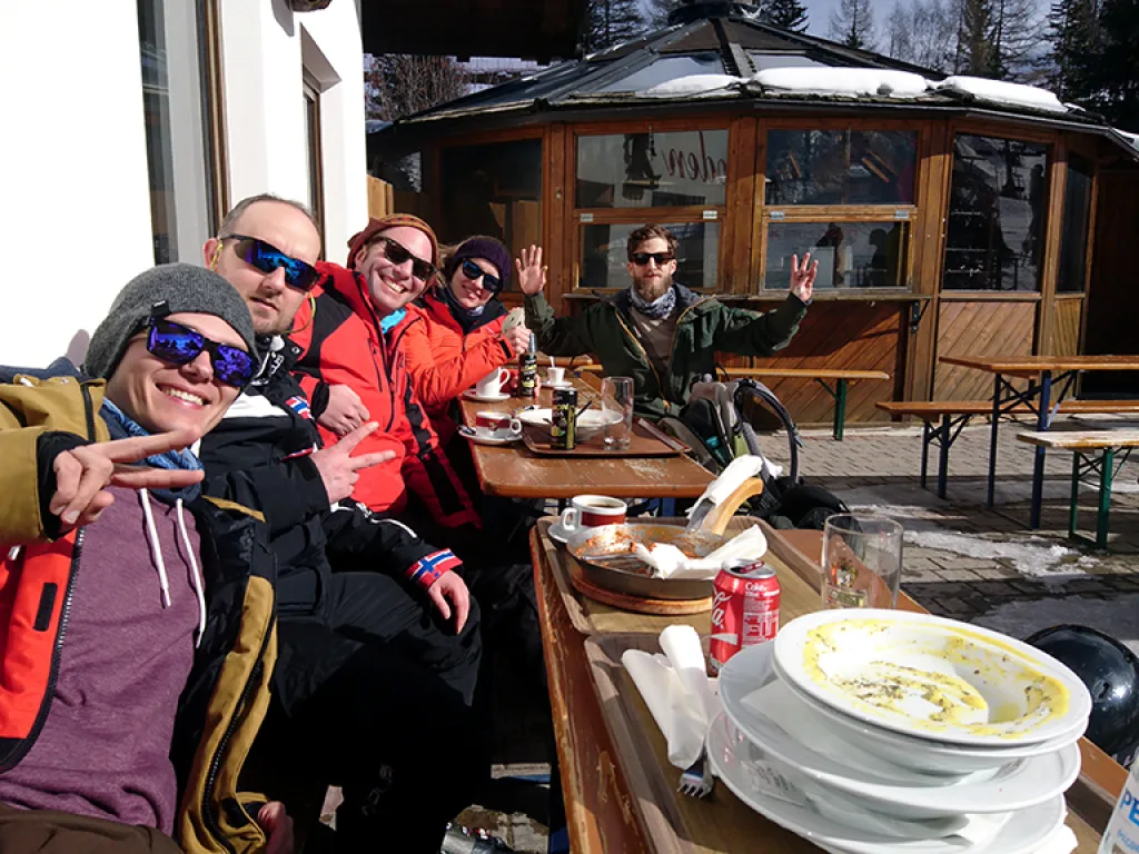 Gruppe sitzt auf der Terrasse einer Hütte beim Essen.